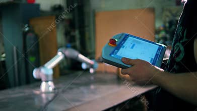 A person uses tablet to control a working robotic arm.