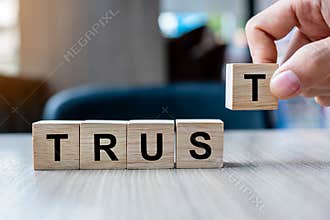 Businessman hand holding wooden cube block with TRUST business word on table background. Trustworthy, Truth, beliefs and agreement
