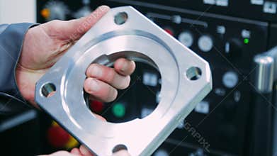 Worker holding steel part in hands. Workerman checking metal part for defects