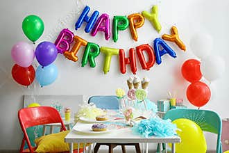 Table with treats and phrase HAPPY BIRTHDAY made of colorful balloon letters