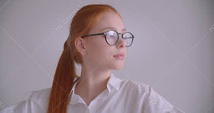 Closeup portrait of young cute caucasian redhead female looking at camera putting on her glasses smiling cheerfully