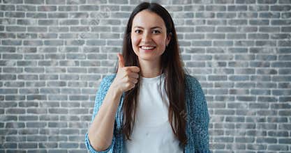 Portrait of happy student showing thumbs-up smiling on brick wall background