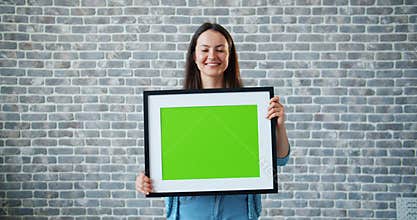 Portrait of beautiful girl holding green chroma key mockup picture and smiling