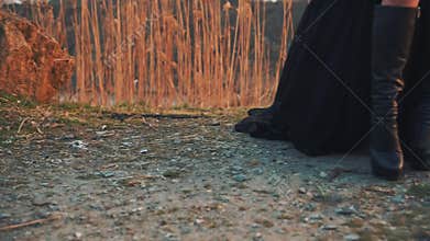 Mysterious stranger in high black leather boots and a dark light flying dress stands on the ground in mountainous area