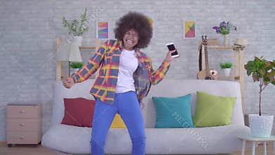 Happy and surprised young African American woman with Afro hairstyle looks at the phone and enjoys winning slow mo