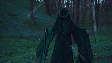 Witch in a emerald raincoat, magician with long curly hairs in spring forest
