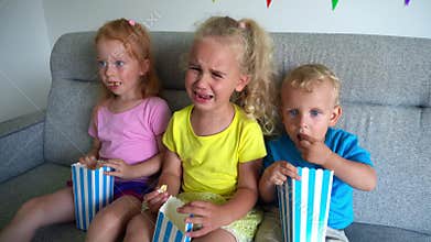 Children eating popcorn and crying. Sad kids watching drama movie on home cinema