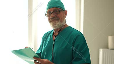 Smiling gray-bearded doctor holding a file with the patient`s medical history. Medicine and healthcare concept