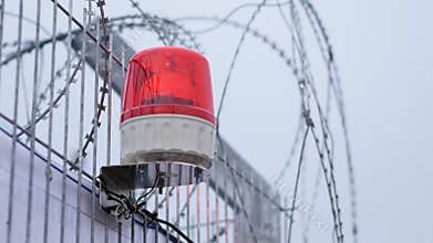 Warning rotating siren flashing lights of signalization at a day. Barbed wire fence with red alarm light