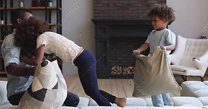 Carefree african dad and kids playing pillow fight on couch