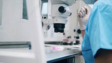 Chemistry lab worker is filling a tube with substance under a microscope