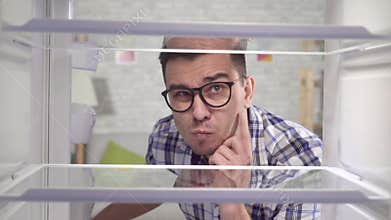Thoughtful young man looks into the empty fridge