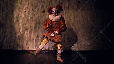 Crazy scary clown dancing against a dark red wall in darkened room.