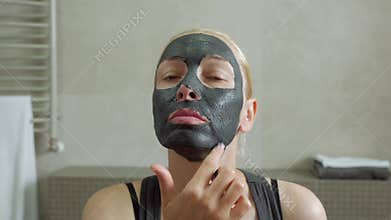 The woman puts a mud mask on a face. Face care. Mud Spa procedures. Day Spa. Drawing a black mask on the person