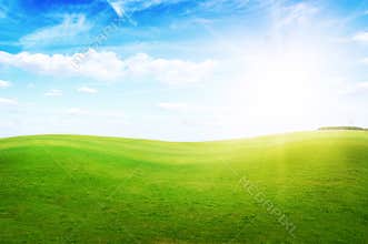 Green grass hills under midday sun in blue sky.