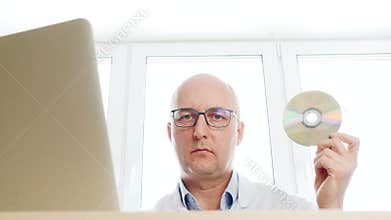 Bio engineer inserting DVD in notebook pc in science lab on window background. Medical worker using CD and notebook in