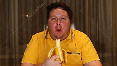 Young fat man eating banana at home