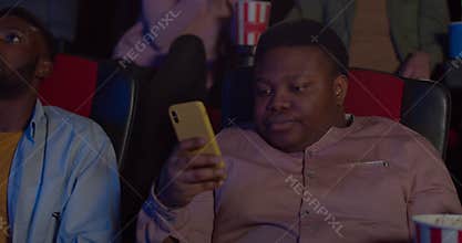 Bored funny guy rolling eyes and looking at phone screen while watching terrible film. Close up of young man using his