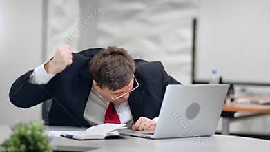 Nervous business man during sudden computer failure sitting on desk in front of broken pc.