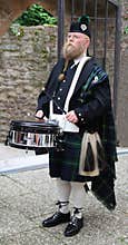 Older man, Scottish, with long beard and kilt, plays on a drum, and drumsticks, he has fu