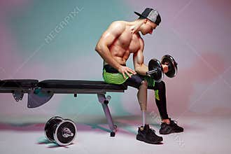 A young muscular man with a disability with a prosthetic leg is training in a gym with dumbbells. Motivation poster.