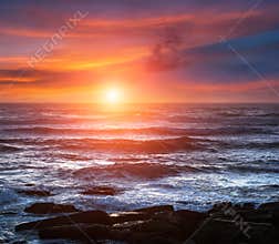 Amazing romantic seascape of ocean coastline at sunset. Landscape of colorful cloudy sky and foamy waves.
