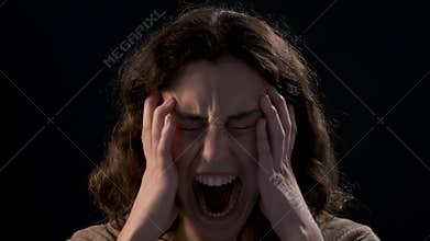 A young woman close-up screaming on black background. Mental illness concept.