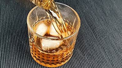 Barman pouring whiskey in the glass with ice cubes on table, focus on ice cubes, whisky relax time on warm