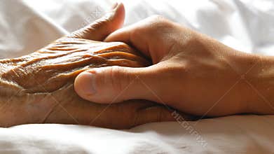 Worried man taking and gently stroking hand of his sick mother showing care or love. Son comforting wrinkled arm of