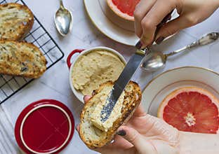 Breakfast on the marble table. girl`s hand holds a bread toast with pate, grapefruits and light chicken pate in a red bowl on the