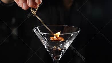 Female bartender setting fire with burning stick on alcohol cocktail in slow motion. Fire ignition on drink with spirit