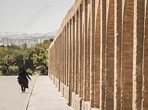 Shape of a woman wearing islamic clothing niqab and veil passing by on the Si o Seh Pol bridge on the afternoon in Isfahan, Iran