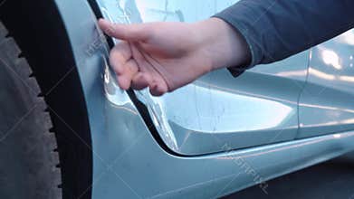 A male hand groping a dent on the door of a wrecked car, checking cracks and paint chips, pressing with a finger, assessing damage