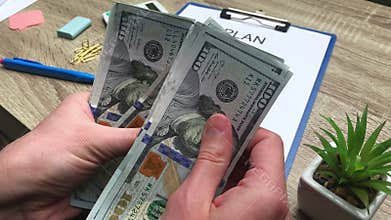 Plan, man counts 100 dollar banknotes at a wooden table