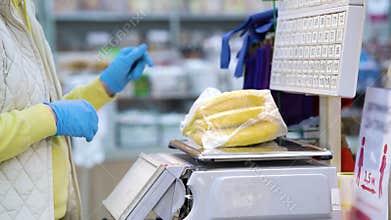 Crop woman in disposable gloves weighing bananas in supermarket