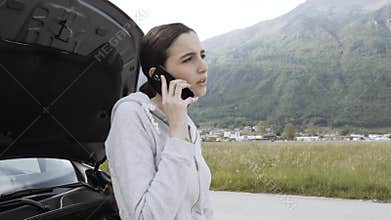 Young woman with broken car calling roadside assistance