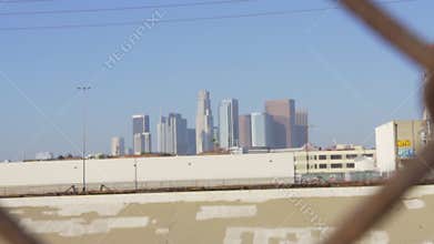 View of Los Angeles downtown skyline through chain link fence on blue sky summer day in slow motion