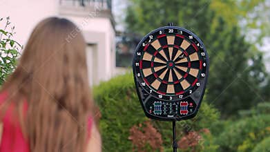 Girl throws a dart at the target. We play darts on the street in the spring garden. Isolation time due to coronavirus.