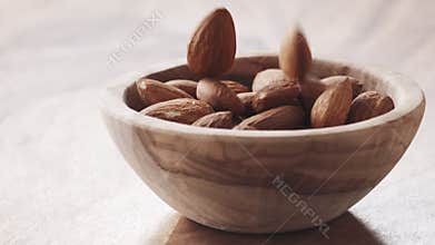 Almonds falling in wood bowl on wooden table in slow motion
