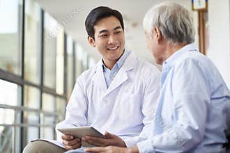 Young asian doctor talking to senior man in hospital hallway