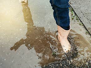 Closeup of girl child pink rain boots in muddy puddle. Seasonal spring summer fall kids activity outdoors. Child having fun