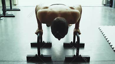 Muscular man working out on dip bars at the gym