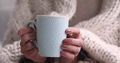 Close up wrinkled female hands holding cup of hot beverage.