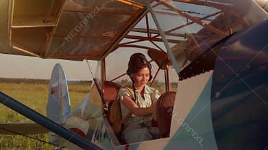 Young adventurous woman pilot in old airplane at summer sunset. Freedom, extreme and feminism concept. Breathtaking