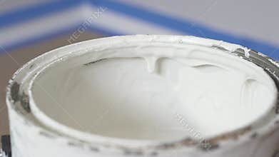 Hand of painter dipping a brush into a bucket with white paint. The paint drips from the brush into the bucket