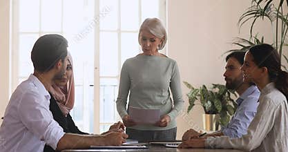 Confident middle aged female team leader holding brainstorming briefing meeting.
