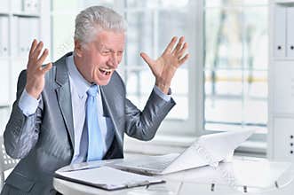 Emotional senior man in formal wear using laptop at office
