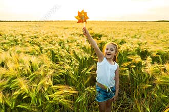 Little girl playing on the meadow on sun with windmill on wheat field