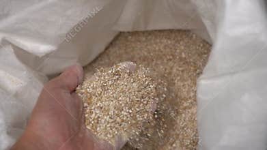 A man`s hand takes the ground beer malt from the bag and slowly empties it.