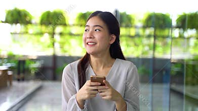 Young 20s Asian beautiful girl walking and holding a mobile phone in window glass building scene.
